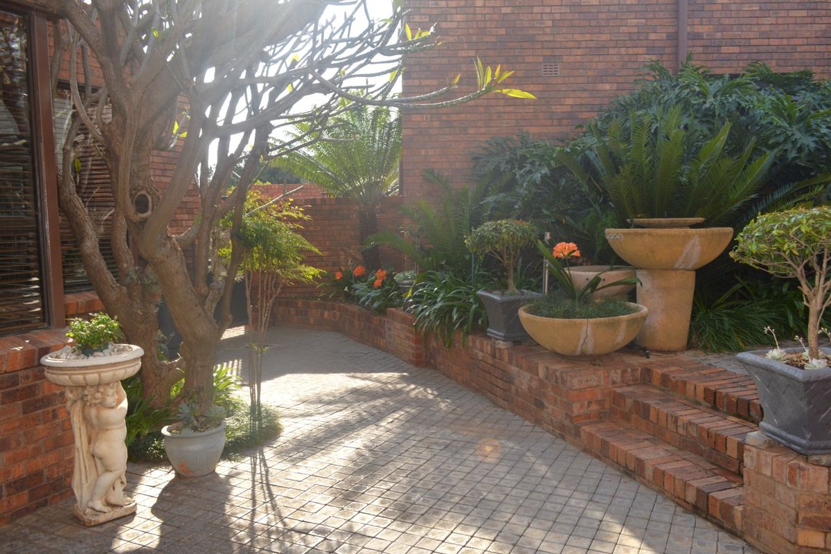 A private rear courtyard featuring brick paving, tiered brick retaining walls, and established garden beds against a classic brick building facade.