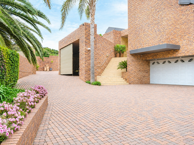 Front exterior view featuring a multi-level brick facade, paved driveway, and a white sectional garage door with an integrated staircase.