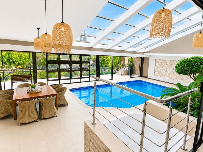 Luxurious indoor pool area featuring a built-in jacuzzi, glass roof for natural light, and elegant tiled finishes, perfect for year-round relaxation and entertainment.