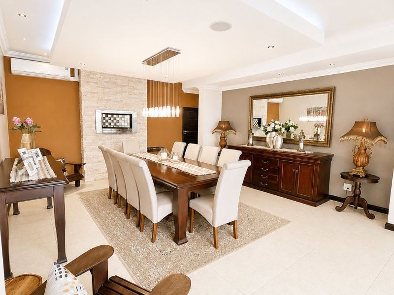 Spacious dining room featuring a stone-clad fireplace, recessed ceiling with cove lighting, and neutral tiled flooring, creating an elegant and well-maintained atmosphere.