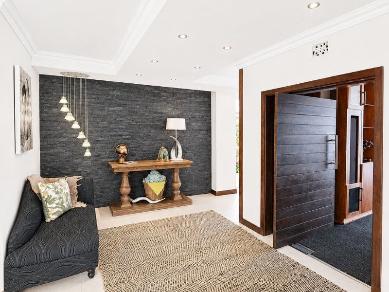 A bright and welcoming entrance hall featuring a striking dark stone feature wall, recessed ceiling lighting, and elegant crown molding.