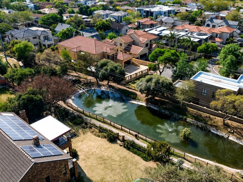 Aerial view of the property featuring a tiled roof with installed solar panels, overlooking a landscaped garden with a fenced pond and water fountain.