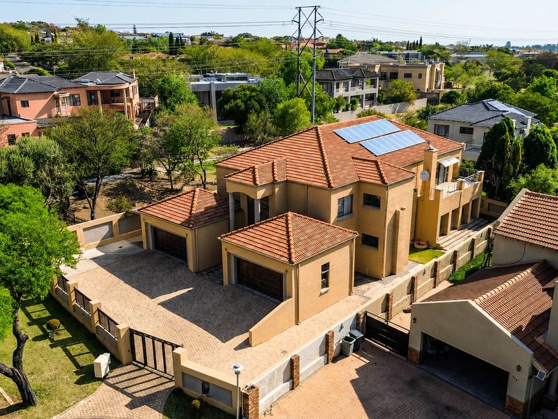 Aerial view of a residential property featuring a tiled roof with solar panels, a paved driveway, and a double garage within a secure boundary.