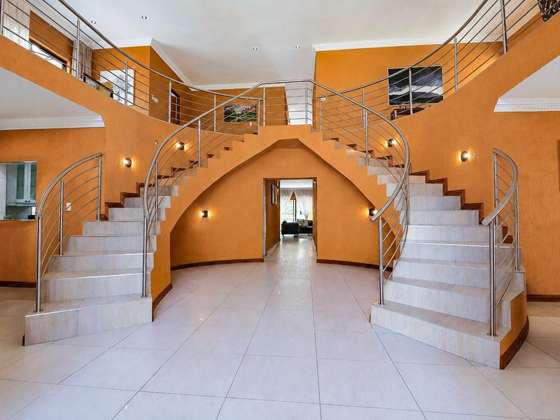 Grand entrance hall featuring a symmetrical double staircase with stainless steel balustrades and polished tile flooring.