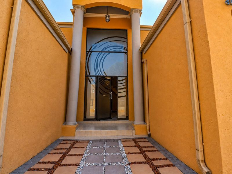 The front entrance features a grand doorway with decorative glass, flanked by structural columns and a paved walkway leading to the tiled entry.