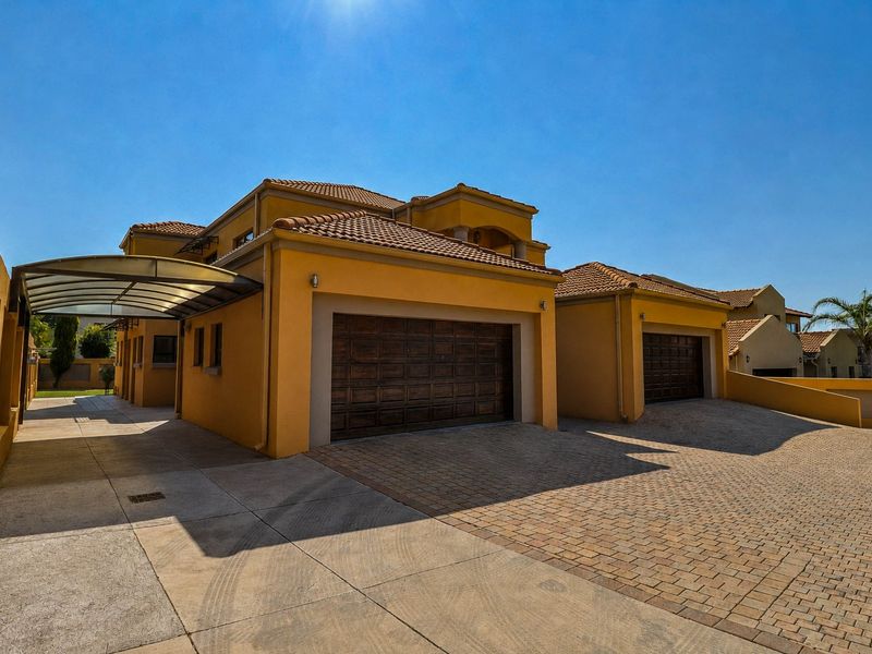 A well-maintained residential property featuring a double garage, paved driveway, and a covered carport area under a tiled roof.