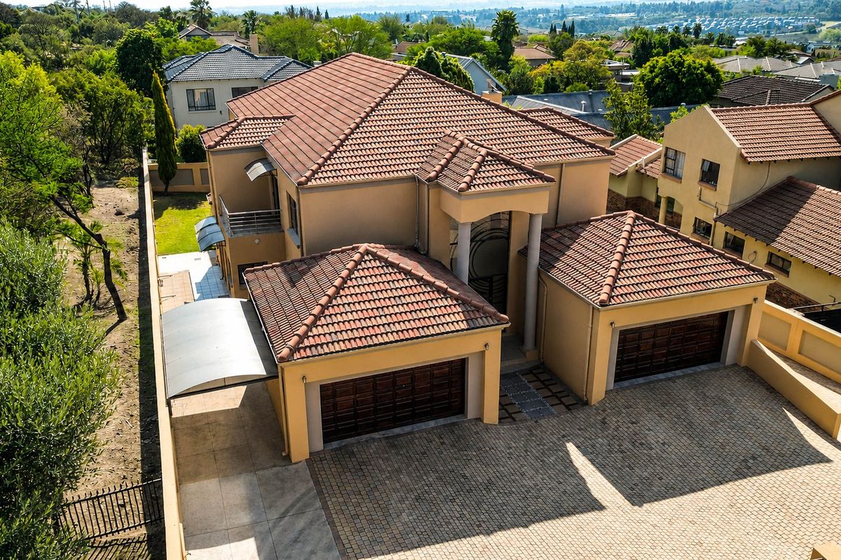 Aerial view of a multi-story residential property featuring a double garage, paved driveway, and tiled roof within a suburban estate setting.