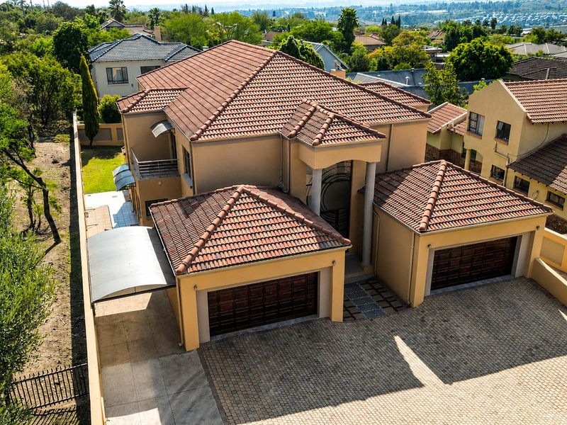 Aerial view of a multi-story residential property featuring a double garage, paved driveway, and tiled roof within a suburban estate setting.