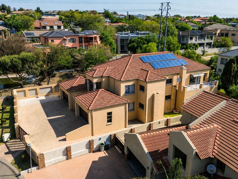 Aerial view of a residential property featuring a tiled roof with solar panels, a paved driveway, and a double garage within a suburban estate.