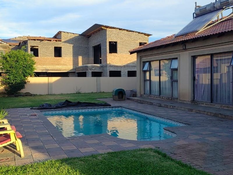 Rear garden area featuring a swimming pool, paved patio, and solar water heating system installed on the tiled roof.