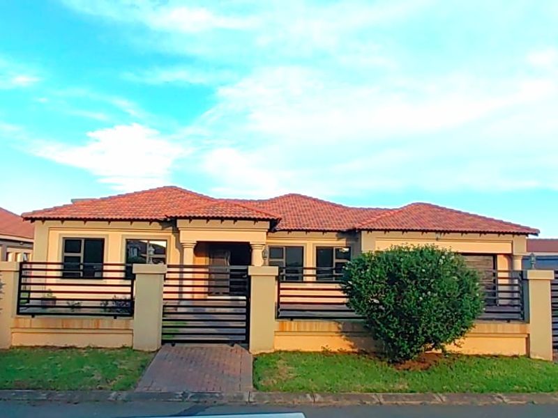 Front elevation of a single-story residential home featuring a tiled roof, perimeter wall with metal gates, and paved entrance walkway.
