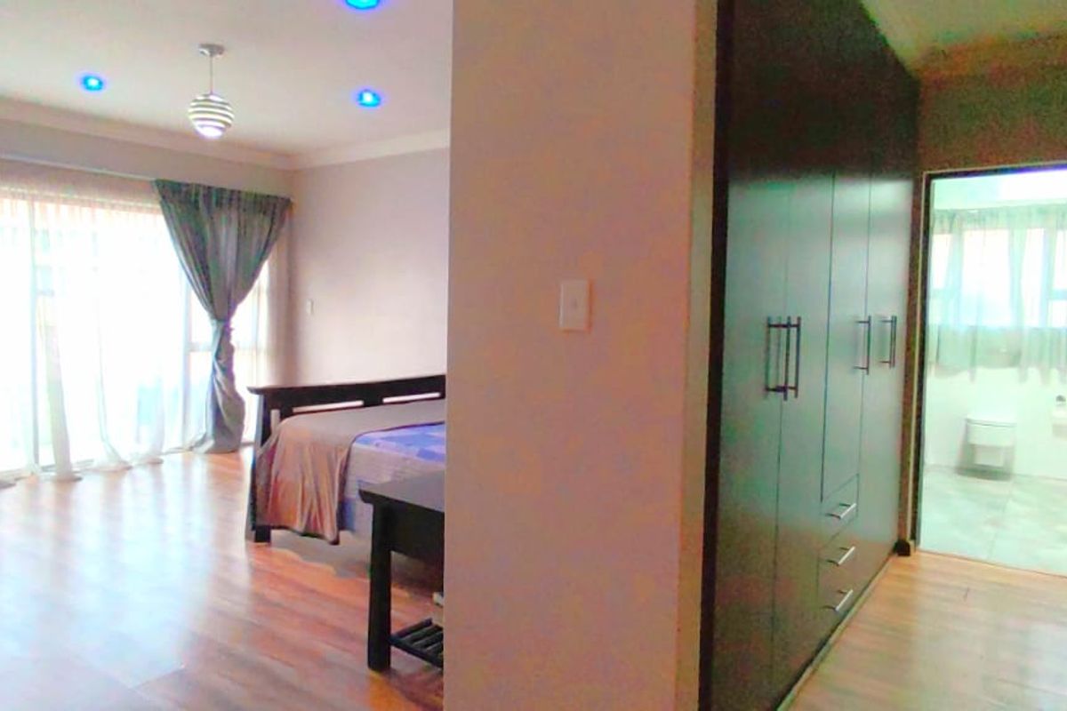Spacious bedroom featuring laminate flooring, built-in cupboards, and sliding glass doors leading to an outdoor area, with an adjoining en-suite bathroom.