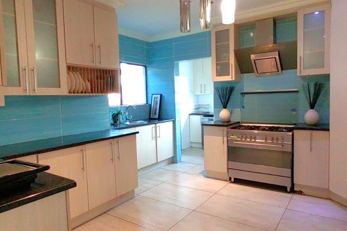 A functional kitchen featuring light-toned cabinetry, granite countertops, a stainless steel gas stove with extractor fan, and a tiled backsplash.