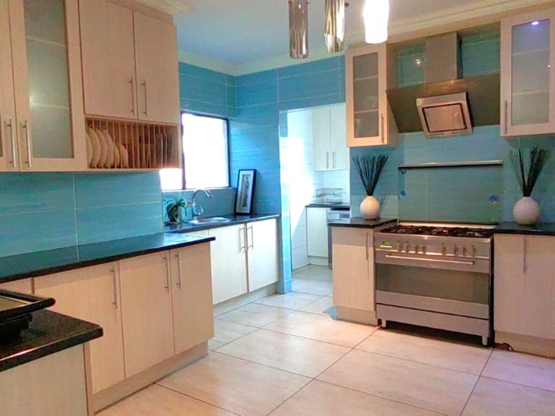 A functional kitchen featuring light-toned cabinetry, granite countertops, a stainless steel gas stove with extractor fan, and a tiled backsplash.
