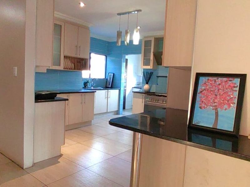 A functional kitchen featuring light-toned cabinetry, dark granite countertops, blue tiled splashbacks, and ceramic floor tiles, with an open-plan layout.