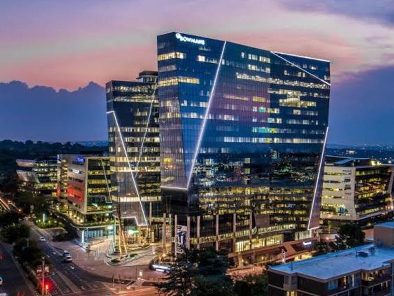 A striking aerial view of a modern commercial office tower at dusk, featuring a glass facade and integrated architectural lighting.