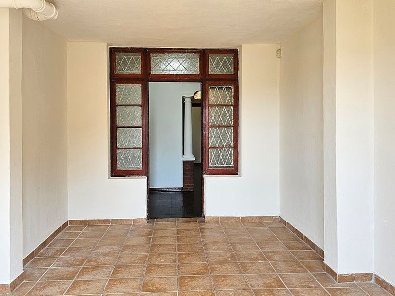 A covered patio area featuring tiled flooring and a traditional leaded glass timber door frame leading into the interior of the home.