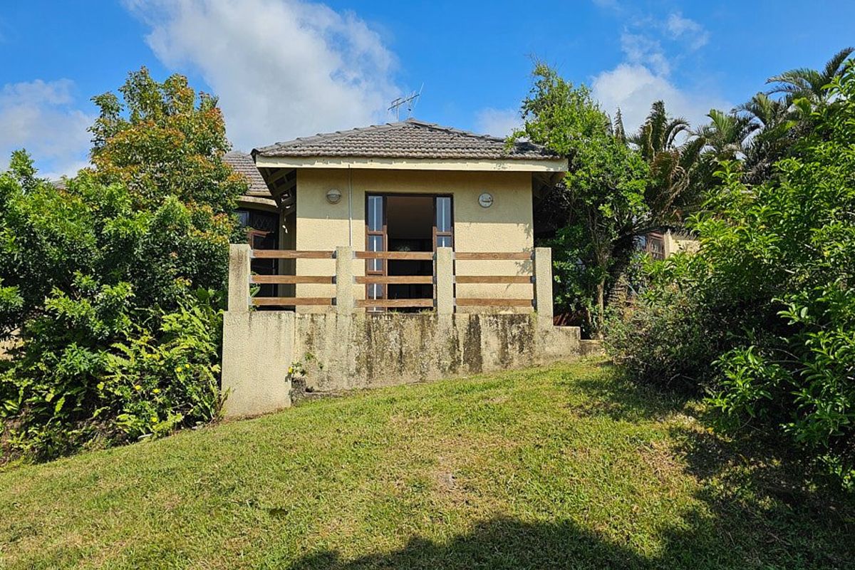 Rear view of the property featuring a raised patio area with a timber balustrade and concrete retaining wall set within a garden.