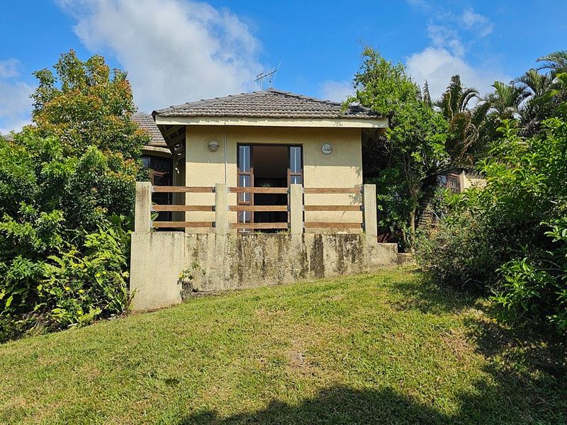 Rear view of the property featuring a raised patio area with a timber balustrade and concrete retaining wall set within a garden.