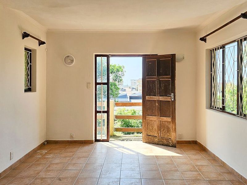 An empty living room featuring tiled flooring, security gates on windows, and a timber door leading to an outdoor area.