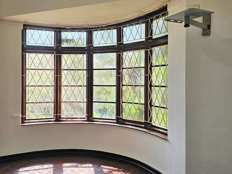 A bright, empty living room featuring a large curved bay window with timber frames, security bars, and original hardwood flooring.