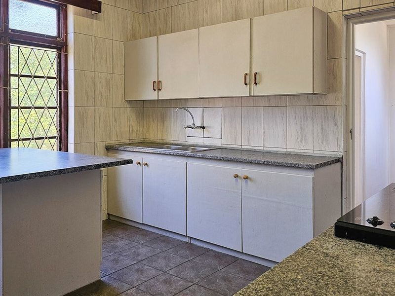 A dated kitchen featuring built-in cabinetry, laminate countertops, a stainless steel sink, and a built-in electric hob with ceramic tiled finishes.