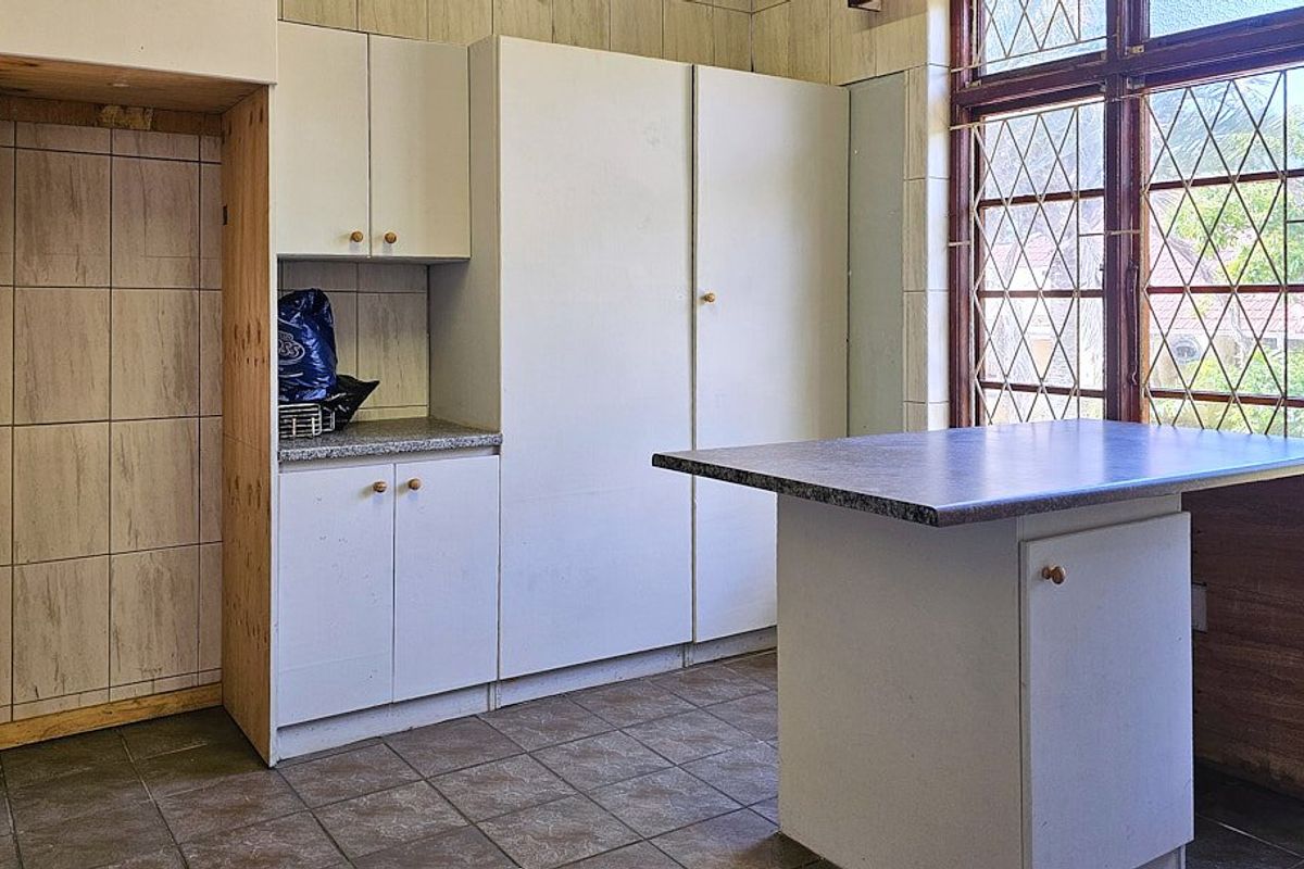 A dated kitchen featuring built-in cabinetry, laminate countertops, and tiled finishes, offering a blank canvas for a modern renovation.