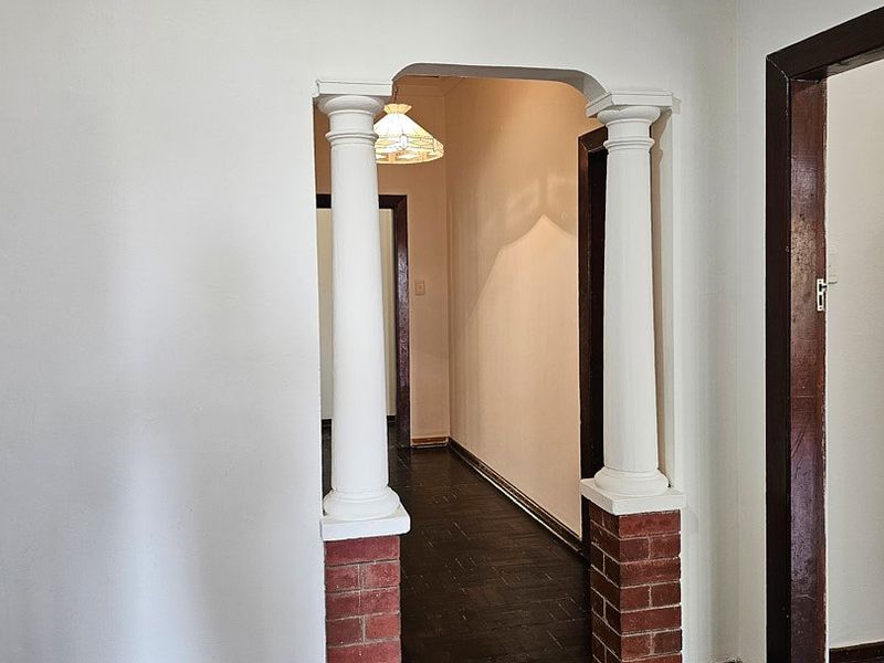 A hallway featuring a decorative arched entryway with brick-based columns and traditional parquet flooring, connecting to adjacent rooms.