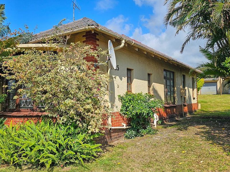 Side view of a single-story house featuring a tiled roof, brick and plastered exterior walls, and established garden surroundings.