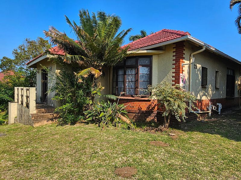 Front elevation of a single-story house featuring a tiled roof, brick accents, and a bay window, set within a garden area.