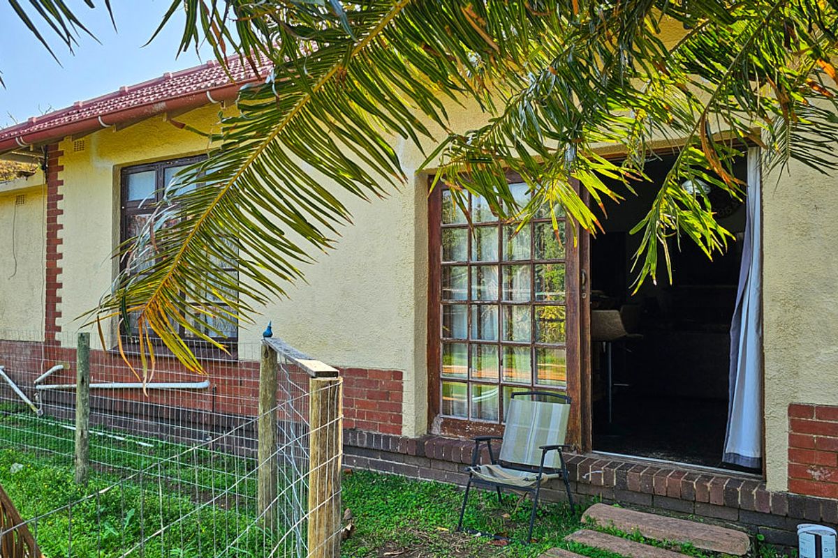Rear exterior view of the house featuring a brick plinth, stucco walls, and timber-framed glass doors leading to the garden area.