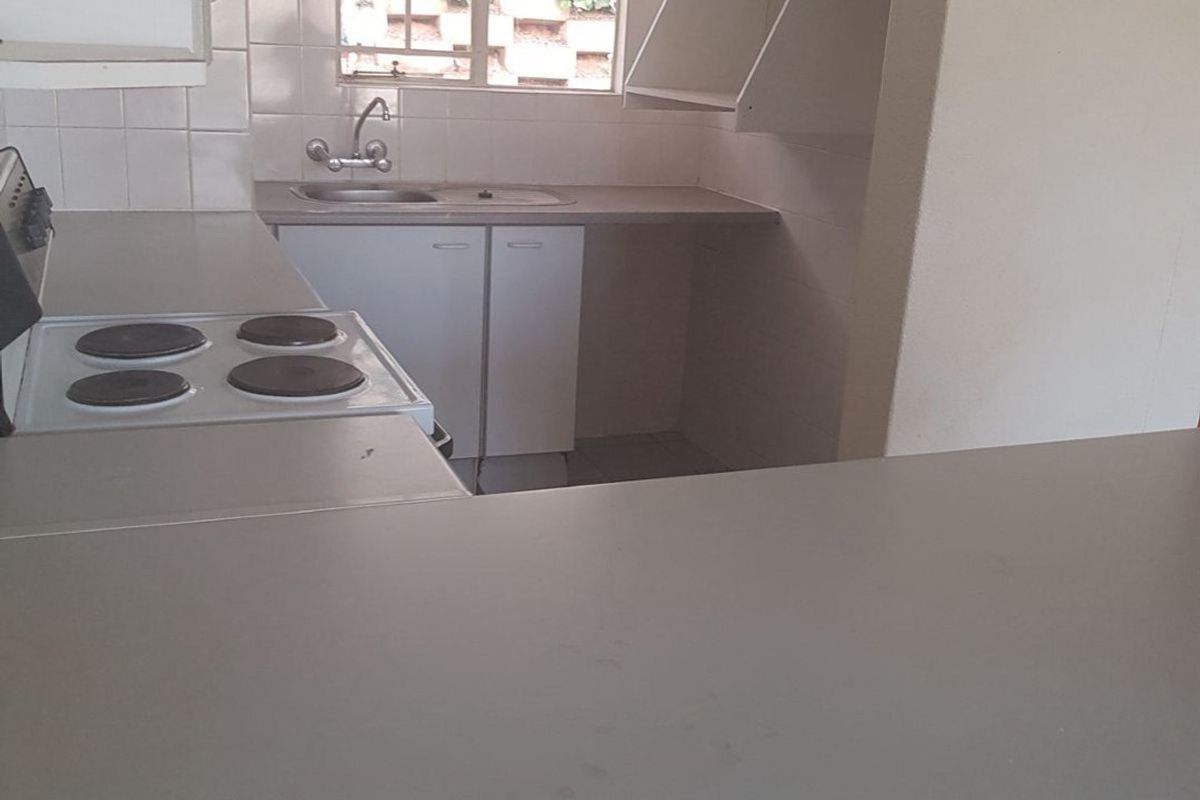 A functional kitchen featuring built-in cabinetry, laminate countertops, a stainless steel sink, and an electric hob, offering a clean and practical workspace.