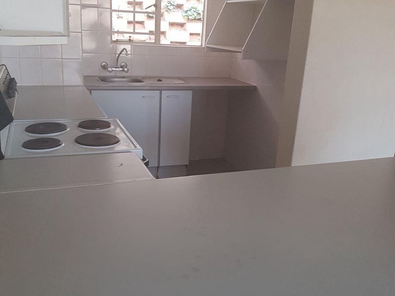 A functional kitchen featuring built-in cabinetry, laminate countertops, a stainless steel sink, and an electric hob, offering a clean and practical workspace.