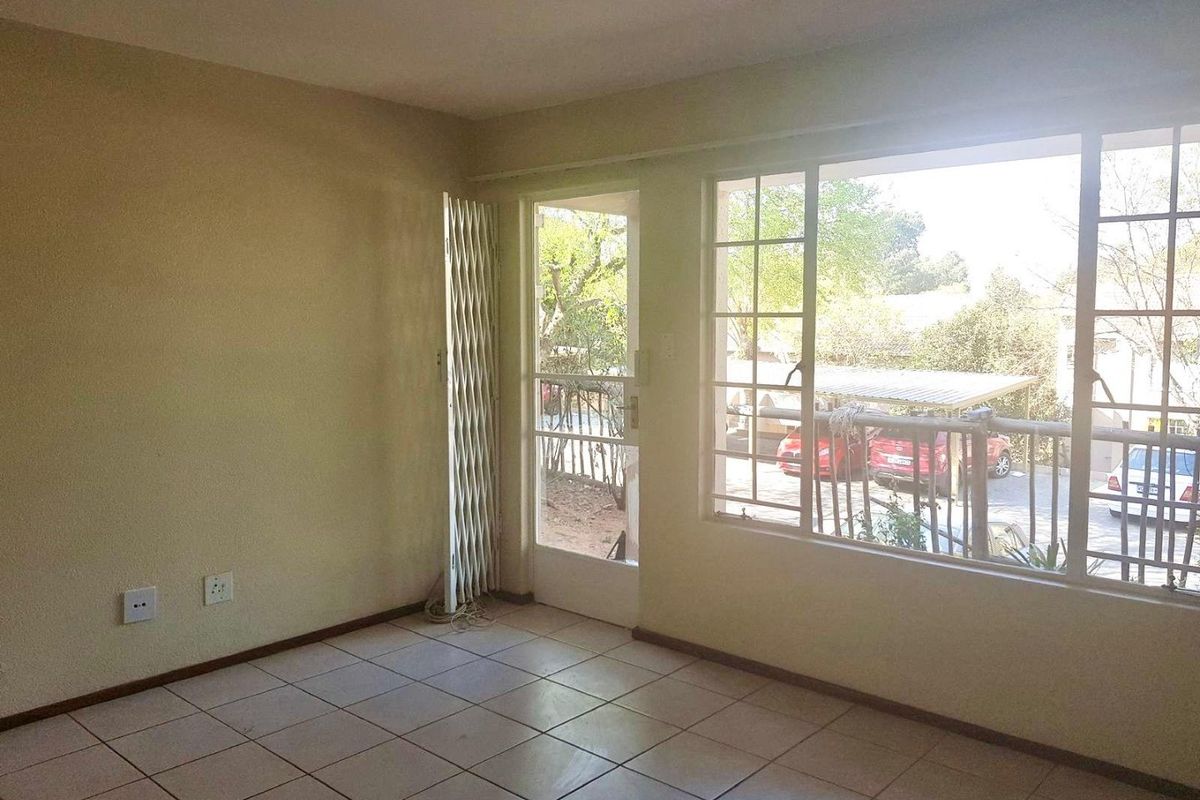 An empty living room featuring tiled flooring, a security gate, and large windows providing natural light and access to the exterior.