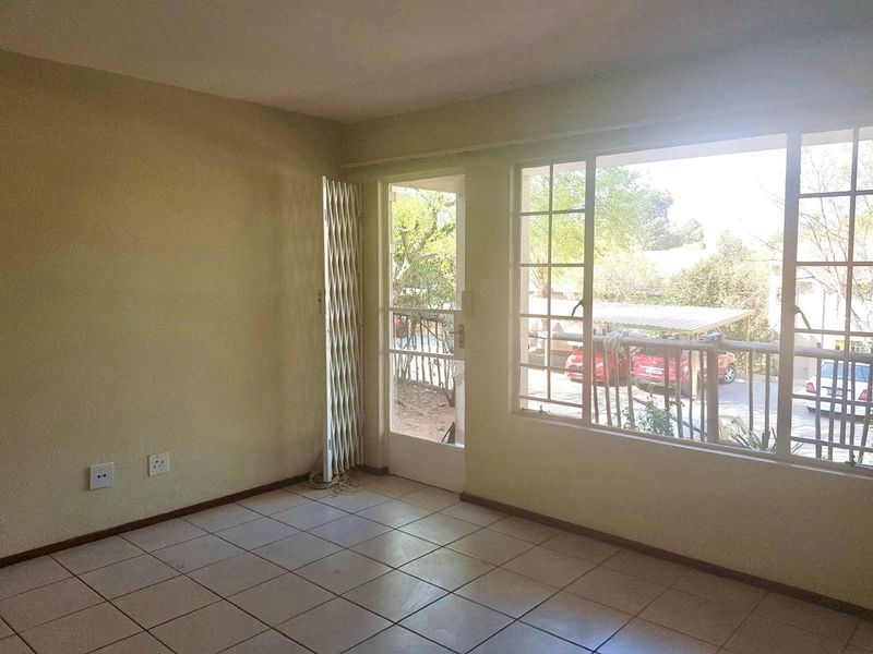An empty living room featuring tiled flooring, a security gate, and large windows providing natural light and access to the exterior.