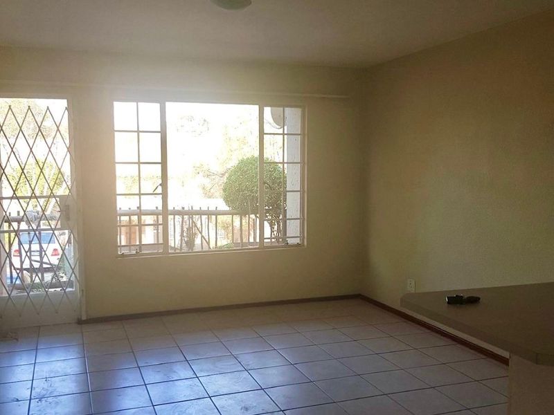 An empty open-plan living area featuring tiled flooring, a security gate, and large windows allowing natural light.
