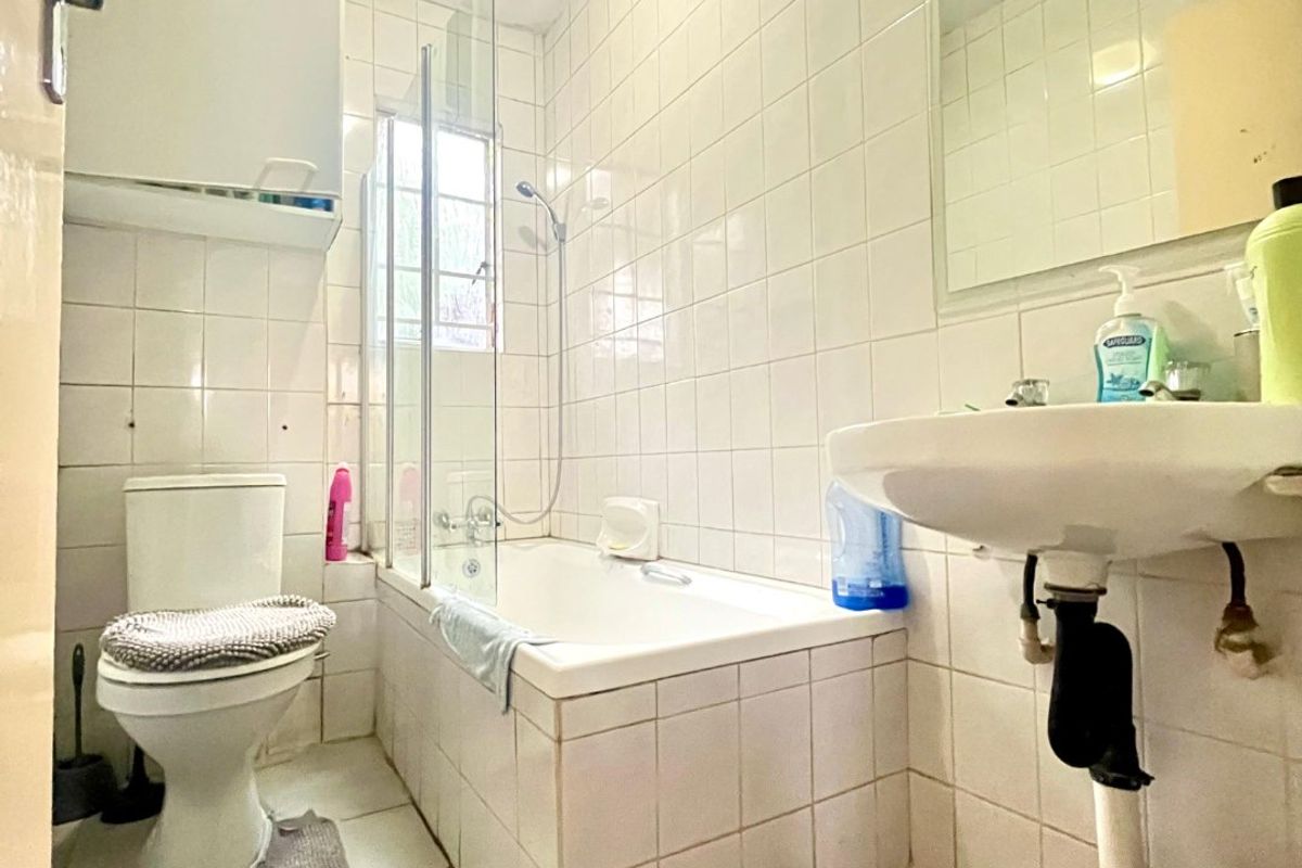 A functional bathroom featuring a bathtub with a glass screen, pedestal basin, and full-height wall tiling, offering a standard layout for an apartment.
