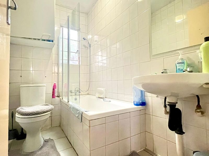 A functional bathroom featuring a bathtub with a glass screen, pedestal basin, and full-height wall tiling, offering a standard layout for an apartment.