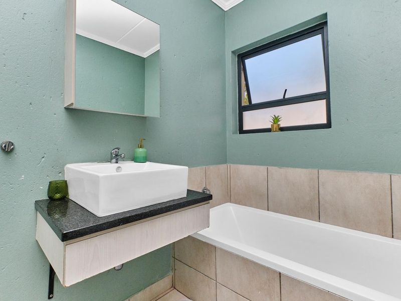 A clean, modern bathroom featuring a vessel sink on a granite vanity, a bathtub, and neutral wall tiling with soft green painted walls.