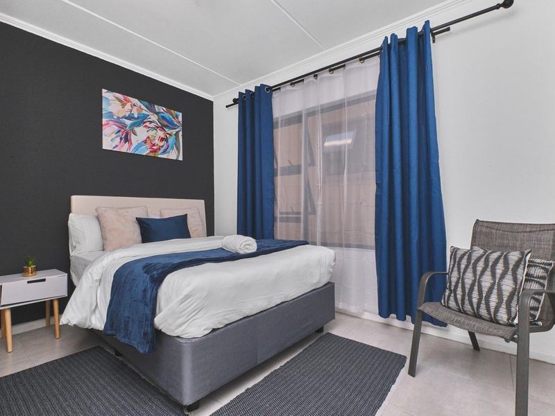 A well-maintained bedroom featuring tiled flooring and a window with a curtain rod, finished with a modern accent wall.