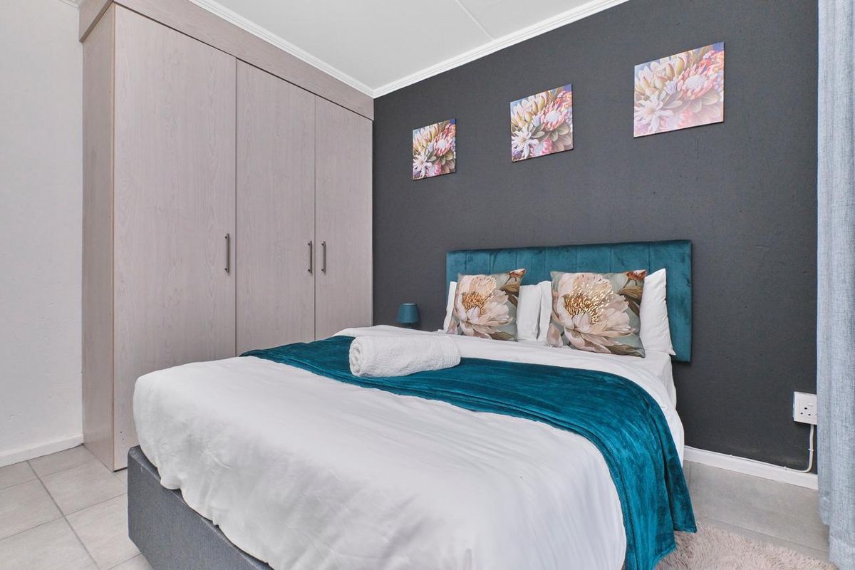 A well-maintained bedroom featuring neutral tiled flooring, a built-in wardrobe, and a dark accent wall.