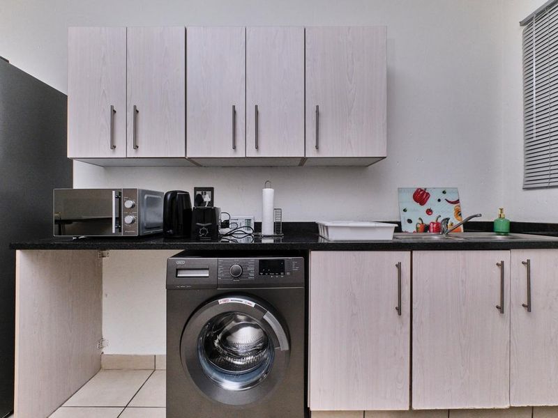 A functional laundry area featuring built-in cabinetry, a granite countertop with an integrated sink, and space for a washing machine.