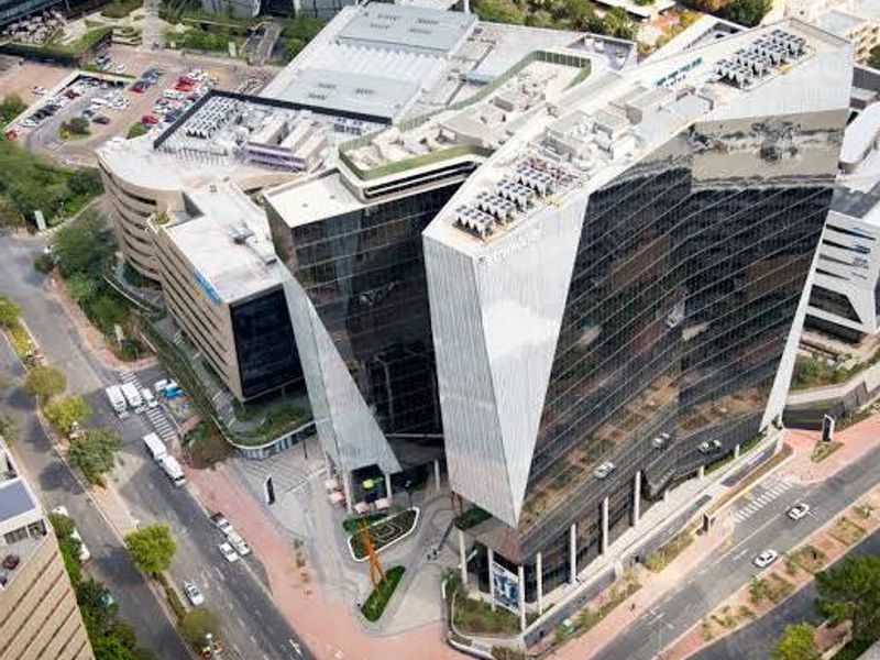 Aerial view of a modern commercial office complex featuring a striking glass facade, rooftop mechanical infrastructure, and integrated pedestrian plaza.