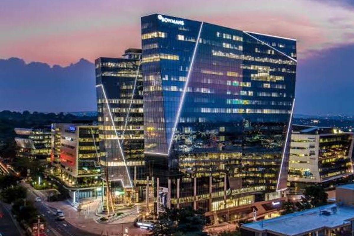 A striking aerial view of a modern commercial office tower at dusk, featuring a glass facade and integrated architectural lighting.