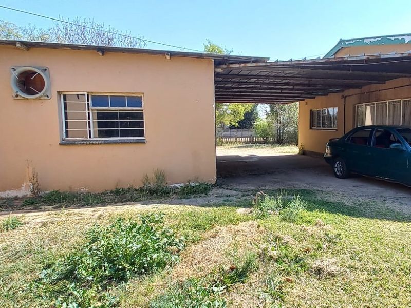 Rear exterior view of the property featuring a carport, security bars on windows, and an attached exterior extractor fan.