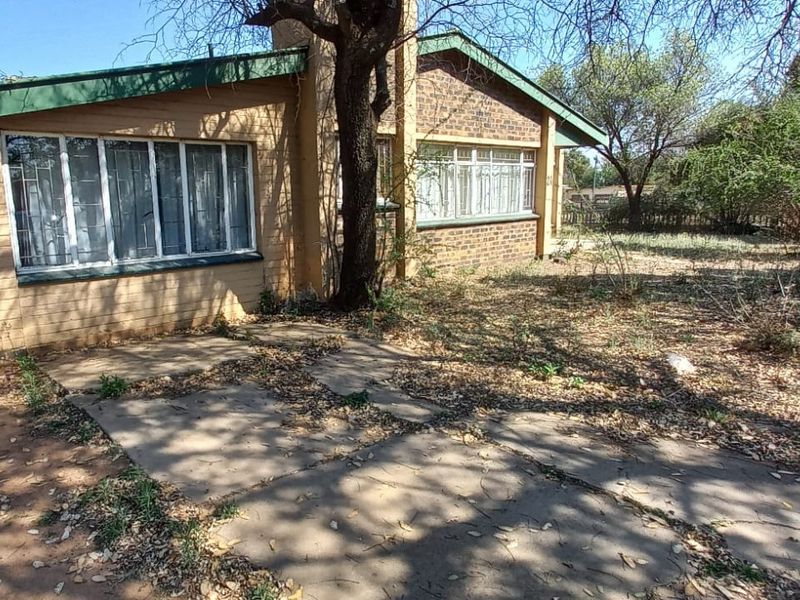 Rear view of the house featuring a brick facade, metal roofing, and a concrete patio area set within an overgrown garden.
