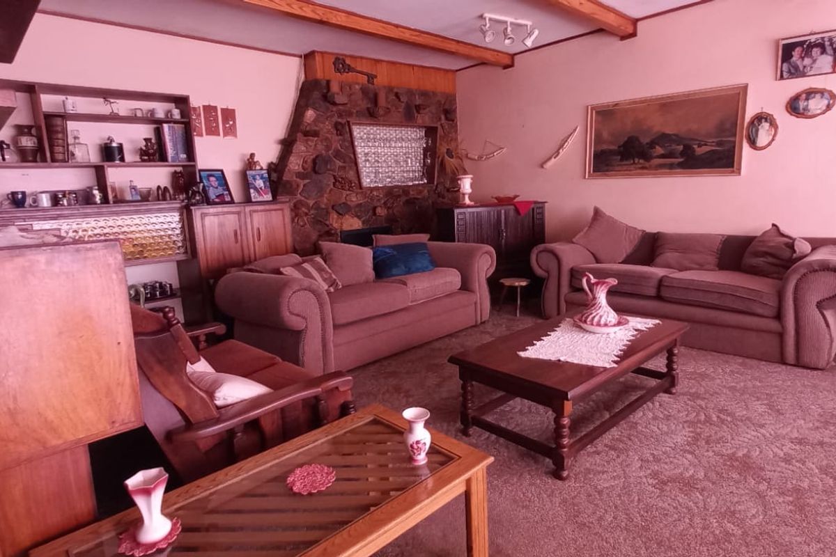Spacious living room featuring a prominent stone fireplace, exposed timber ceiling beams, and built-in shelving, offering a traditional aesthetic with potential for modernization.