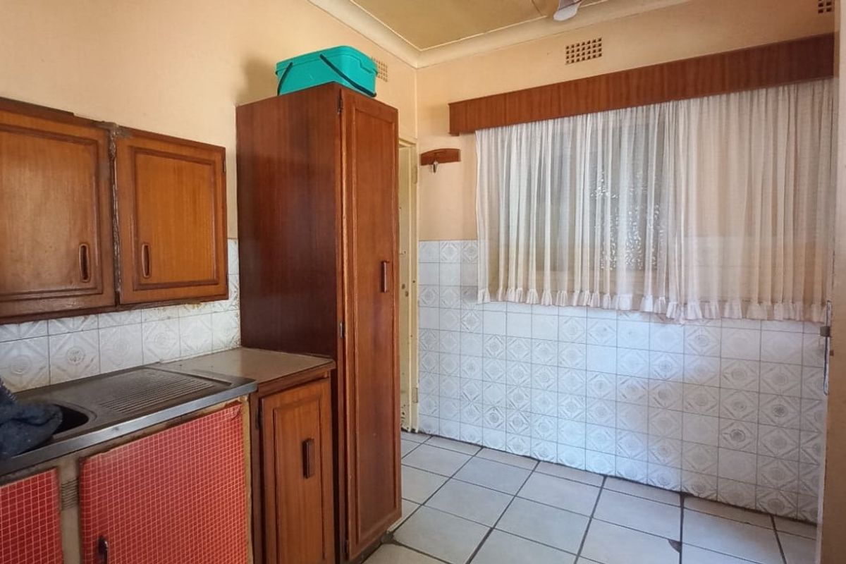A dated kitchen featuring original wooden cabinetry, tiled splashbacks, and tiled flooring, offering significant potential for a modern renovation.