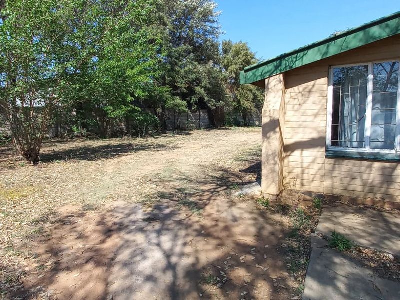 Rear exterior view of the property featuring a large garden area, concrete paving, and a building facade with metal security bars on the windows.