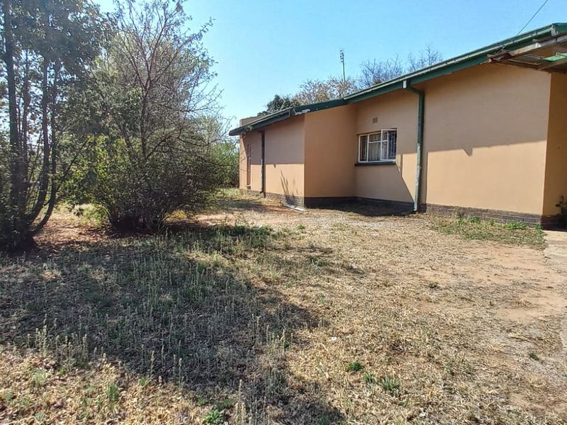 Rear exterior view of the house featuring a carport, concrete driveway, and a large garden area requiring landscaping.